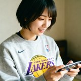 一位留着短发的女性篮球爱好者，穿着NBA湖人队周边卫衣，手中拿着手机正在观看直播